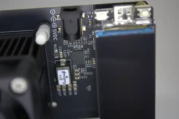 Close-up of NerdAxe Gamma Bitcoin solo miner showing 5 V DC barrel jack, USB-C port and on-board voltage-regulator circuitry next to the OLED display