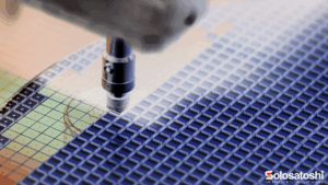 Close-up of a semiconductor wafer covered in repeating chip patterns with a robotic tool positioned over the wafer during manufacturing or inspection.