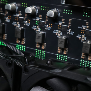 Close-up of NerdOctaxe Gamma Rev 3.1 VRM power delivery section showing FP1008R5 inductors, 220uF capacitors, MOSFETs, and surface-mount components with green LED indicators on black PCB