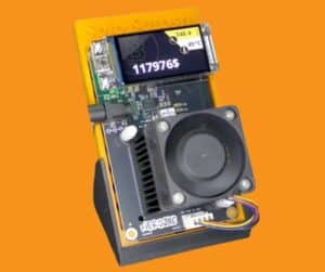 Nerdaxe Gamma Rev 2.3 Bitcoin solo miner on yellow Solo Satoshi stand with 1.9-inch color IPS LCD displaying live Bitcoin price at $117,976 and 49°C ASIC temperature, 40mm fan, and green PCB with NerdAxe Gamma branding